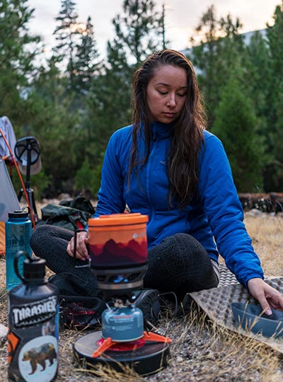 Fotografie Adély sedící u vařiče a připravuje jídlo na plynovém vařiči